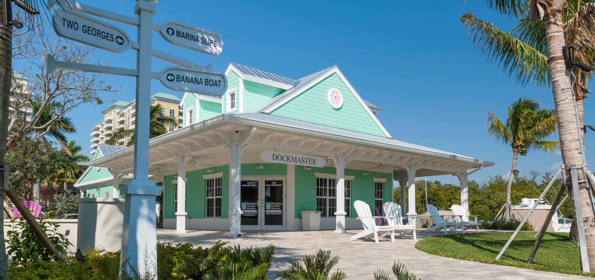 Aqua building with white trim surrounded by landscaping with two Adirondack chairs