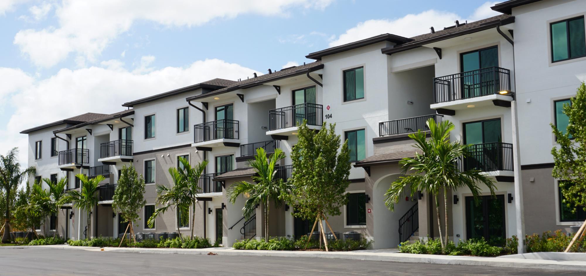 View of 3-story building with white and gray accent painting surrounded by palm trees